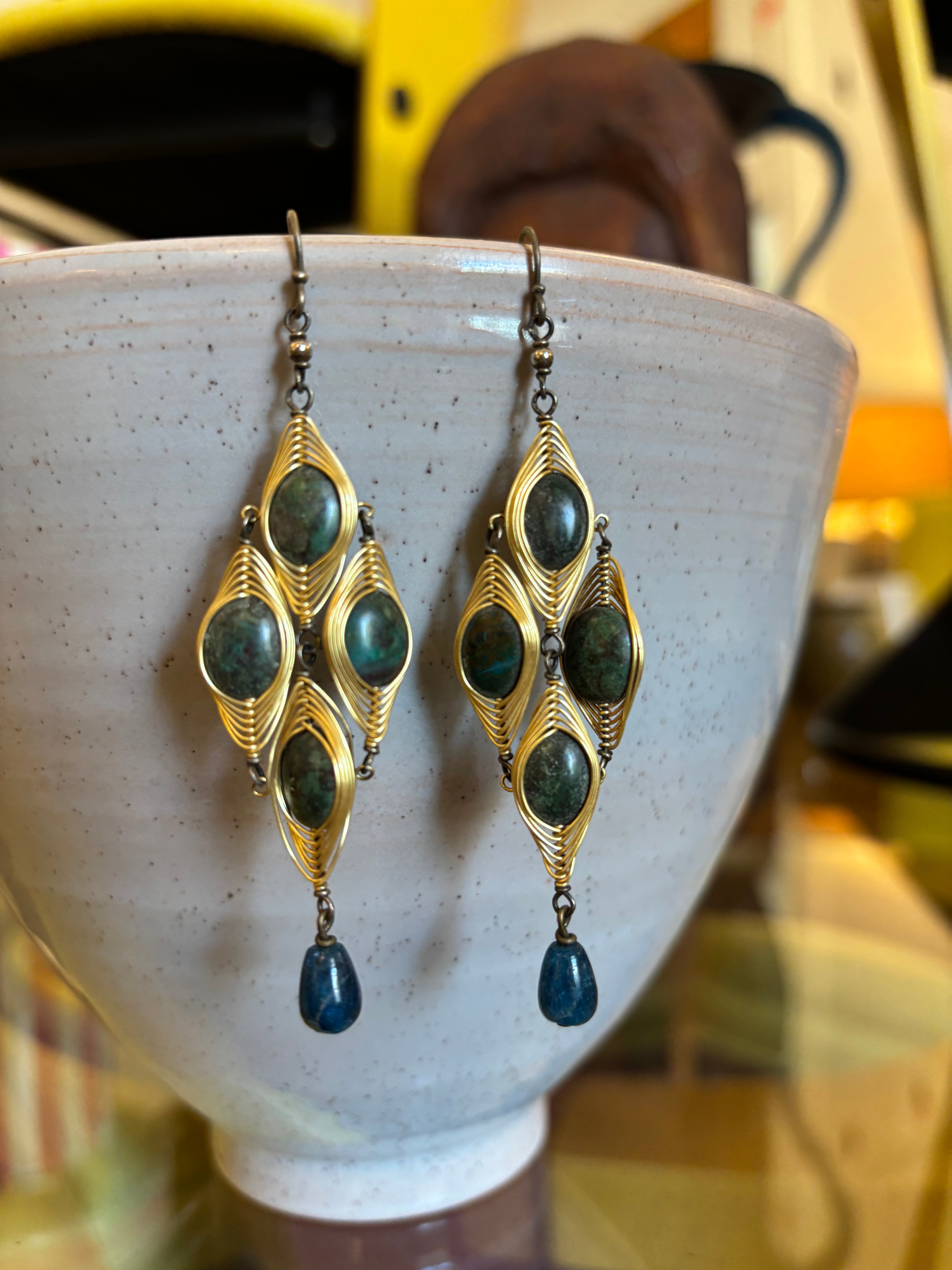 Pair of gold and green gemstone earrings on a white ceramic stand.